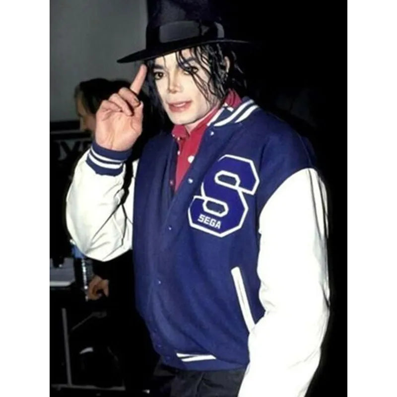 Person wearing a blue and white jacket with a 'S' logo, posing with a finger on their lips.