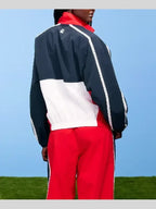 Person wearing a navy, white, and red tracksuit against a blue sky.